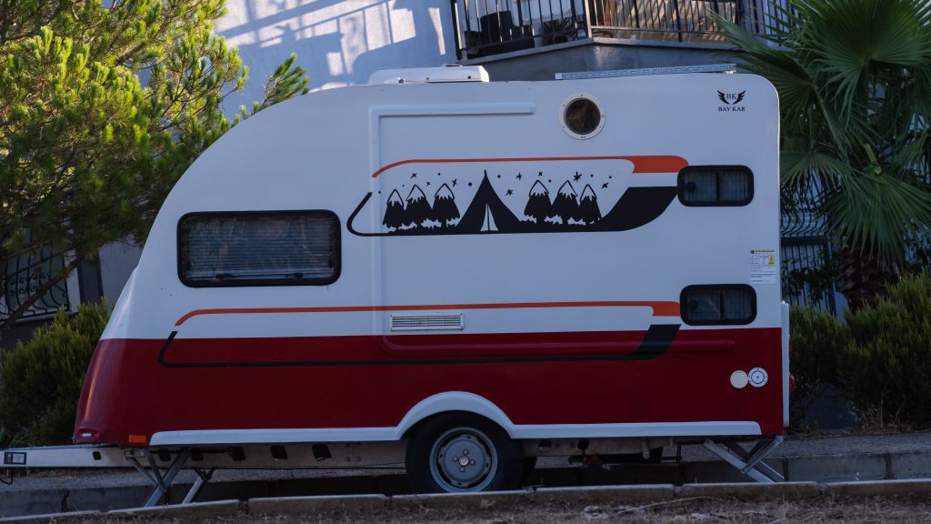 A vibrant red and white caravan with camping graphics parked outdoors in İzmir.
