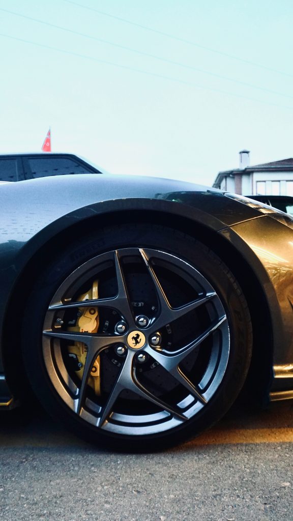 Close-up of a gray luxury sports car parked outside with polished alloy wheels at sunset.